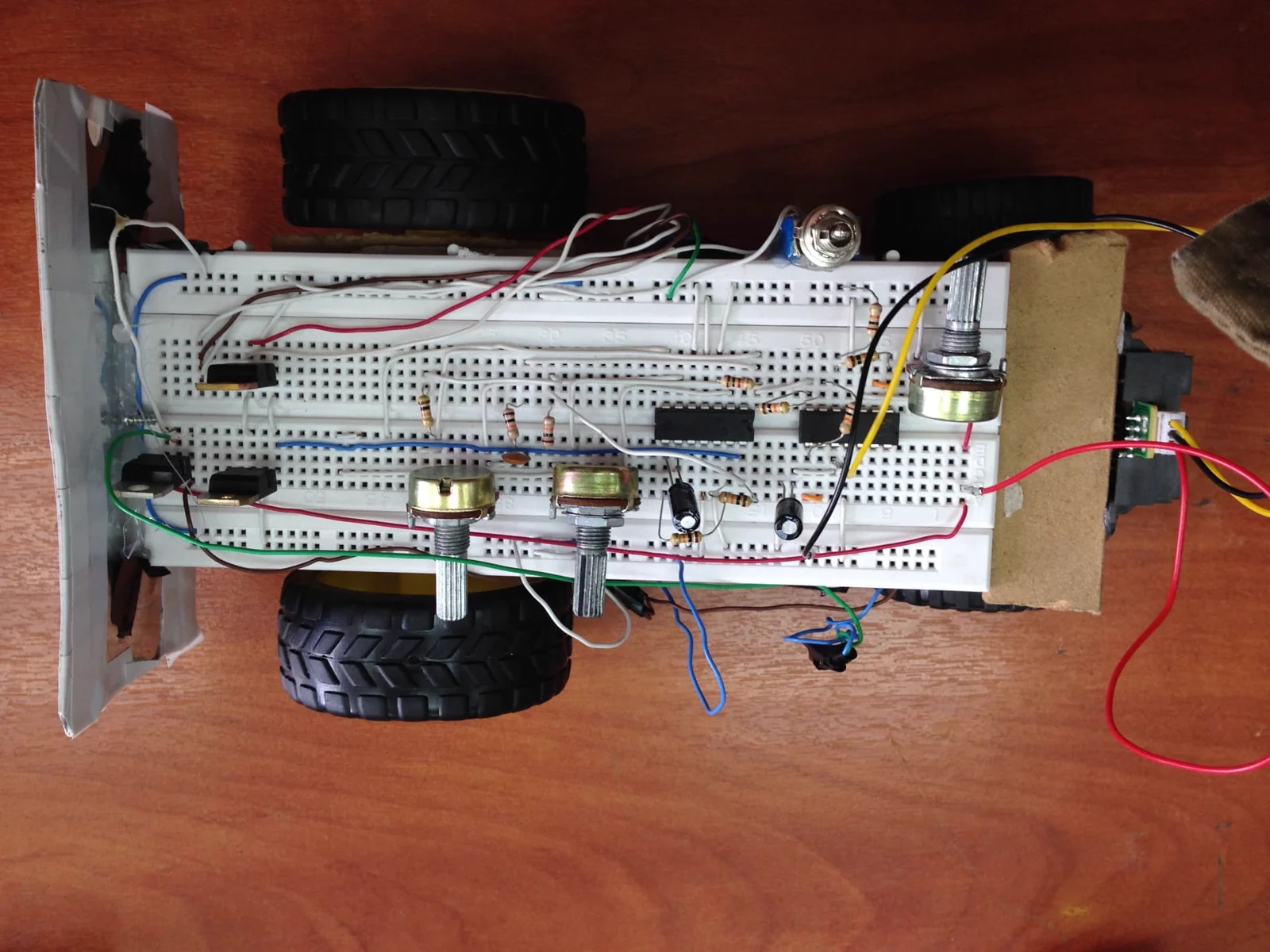 Small breadboard robot vehicle with wheels, potentiometers and a control circuit mounted on the chassis