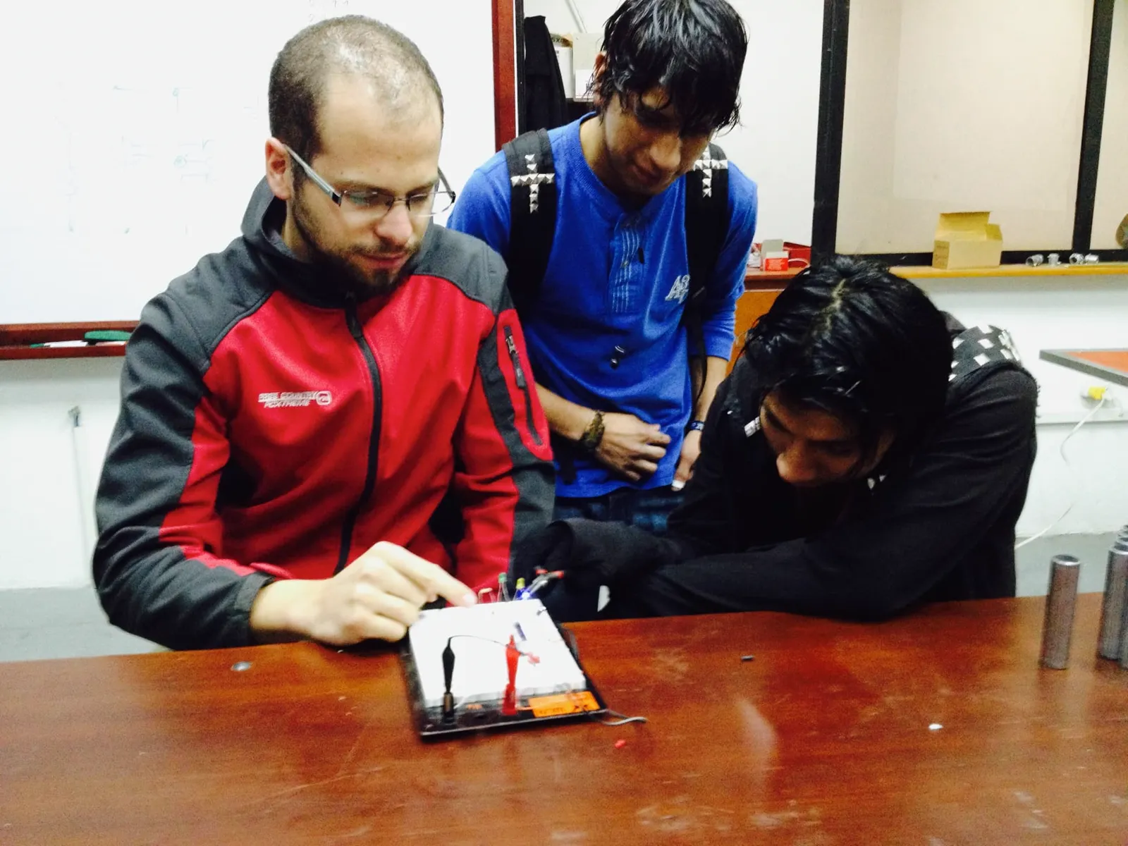 Explaining a circuit board to two students at a laboratory bench