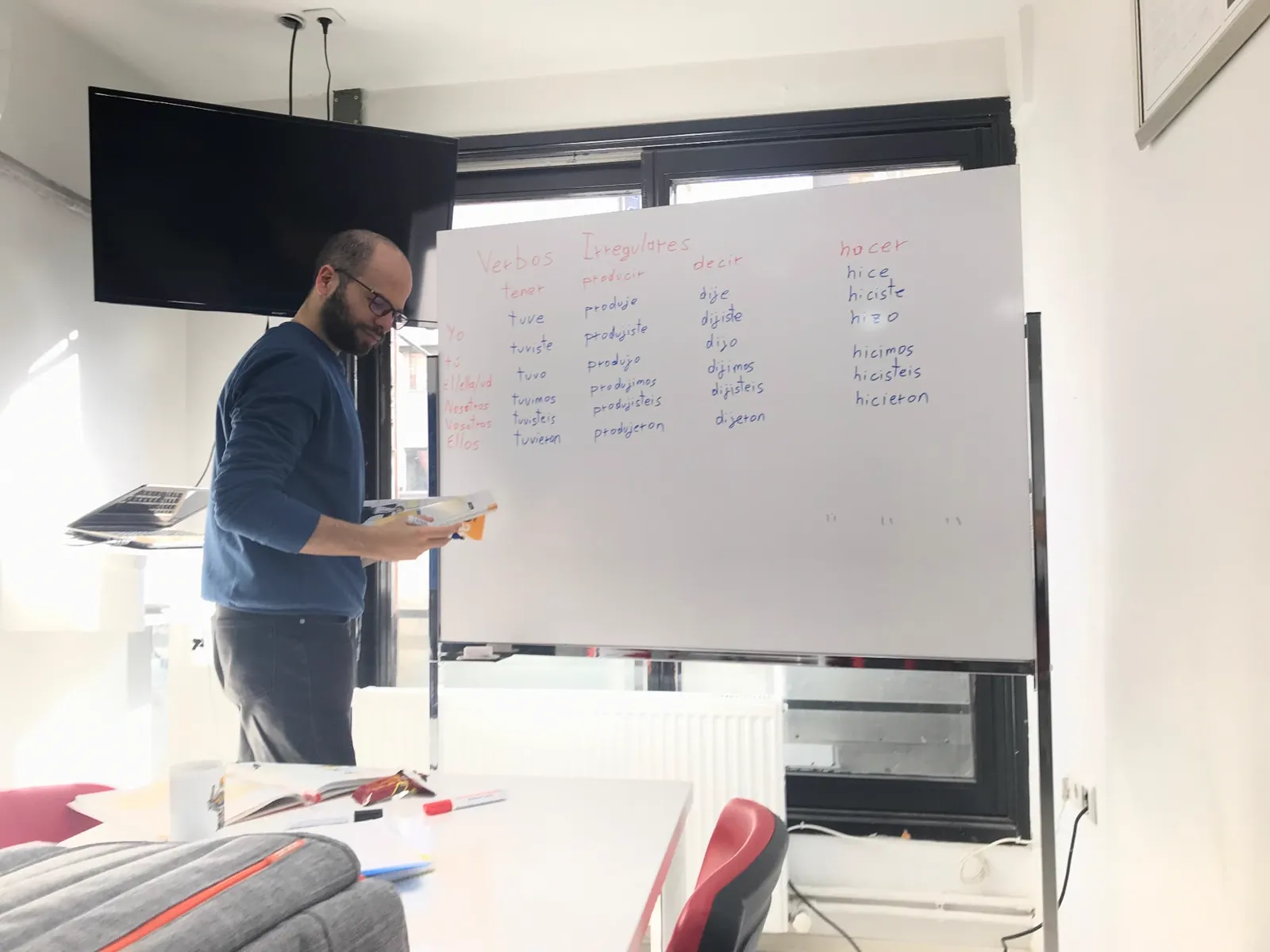 Teaching irregular Spanish verbs at a whiteboard in a bright classroom